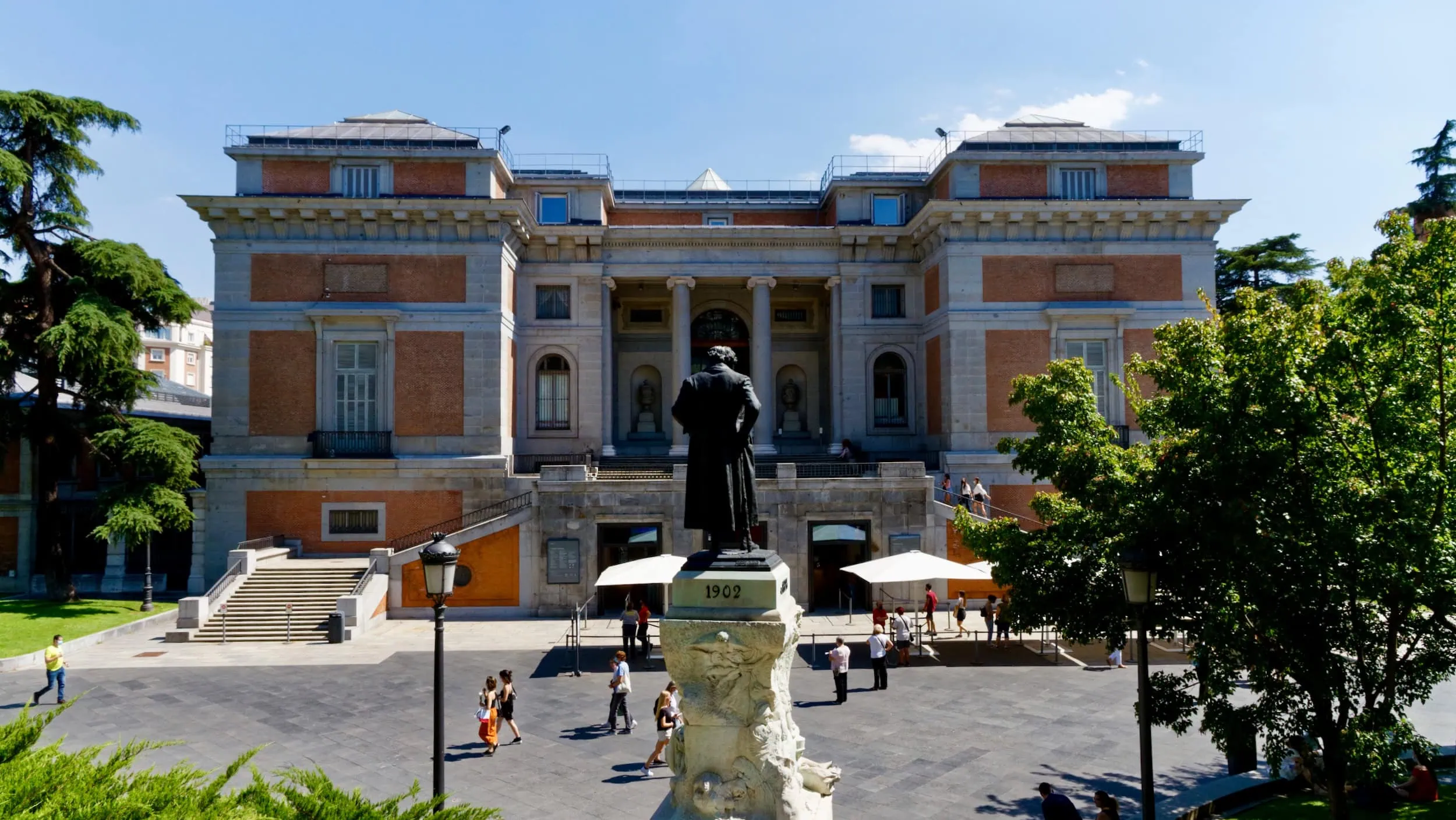 Zijgevel en entree van het Museo Nacional del Prado in Madrid, gezien over de schouder van het standbeeld van Francisco de Goya richting het gebouw van Juan de Villanueva.