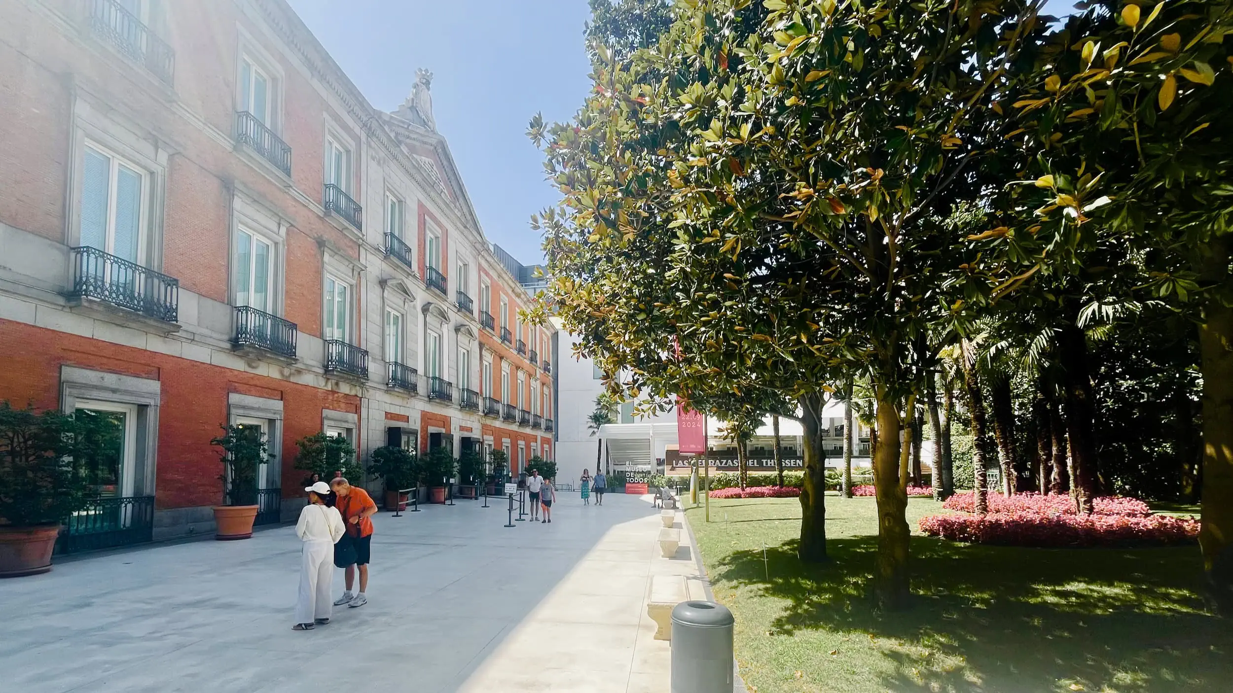 Hoofdentree van het Museo Thyssen-Bornemisza in Madrid met een kleine binnentuin, bezoekers en de toegang tot de museumcafeteria op de achtergrond.