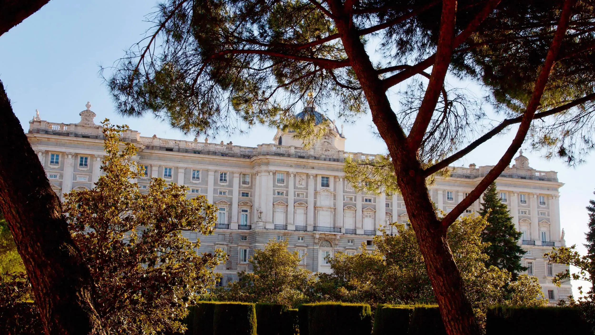 Achterzijde van het Koninklijk Paleis van Madrid, gezien vanuit de Jardines de Sabatini, met zicht op de koninklijke kapel en karakteristieke pijnbomen.