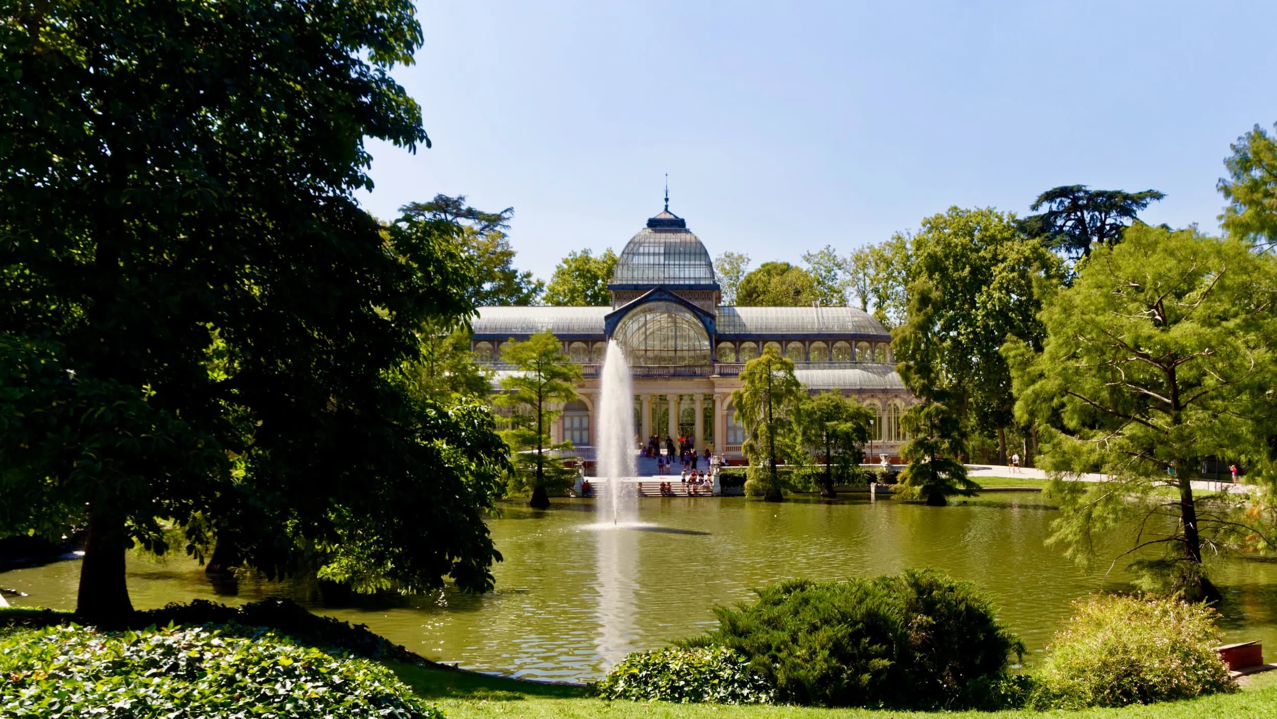 Palacio de Cristal in het Retiro Park met de romantische vijver op de voorgrond en weelderig groen rondom, badend in het licht van Madrid.