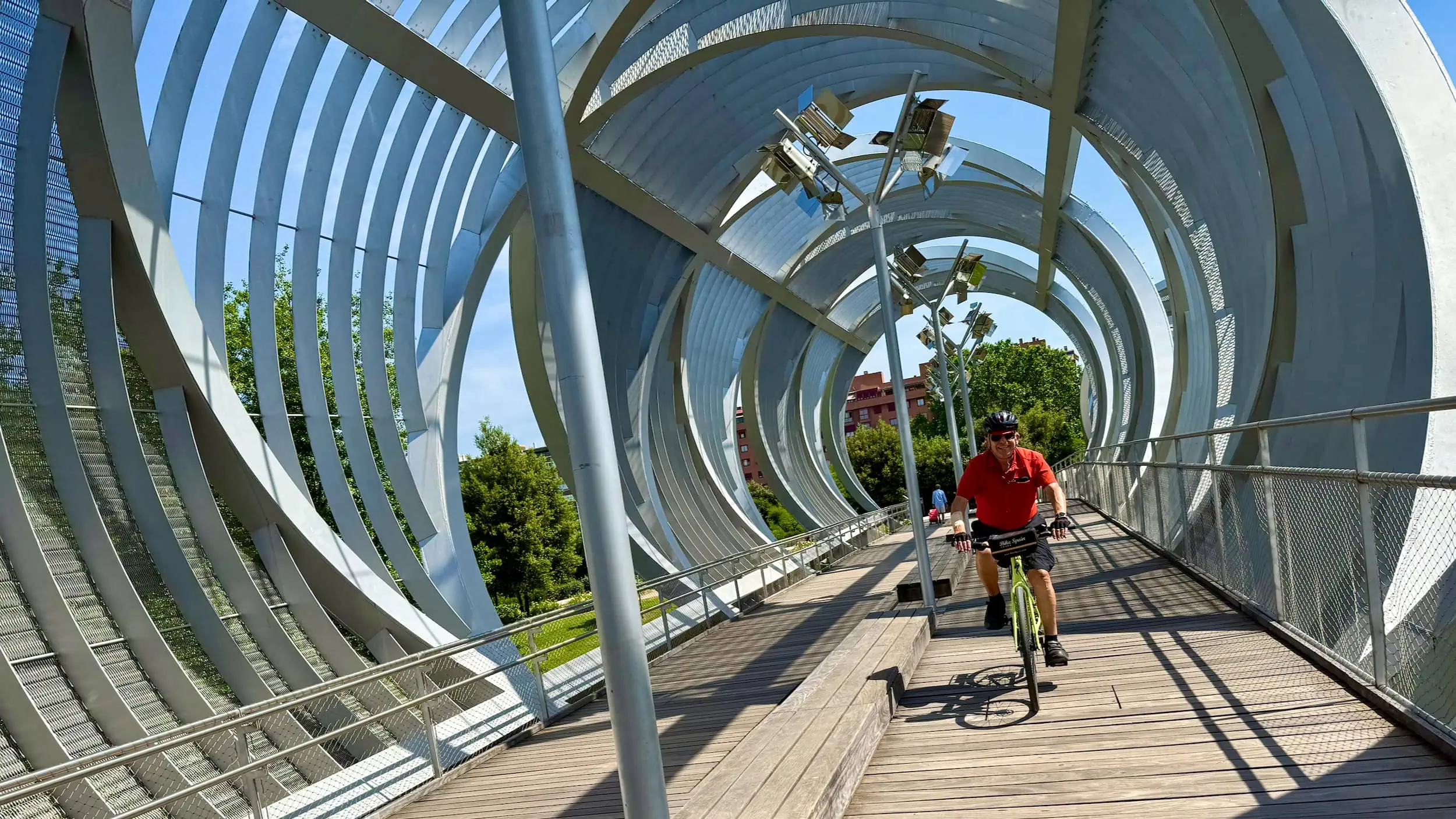 Fietser op de Puente de Arganzuela in Madrid, ontworpen door Dominique Perrault, met de spiraalvormige structuur die zich dynamisch om hem heen ontvouwt.