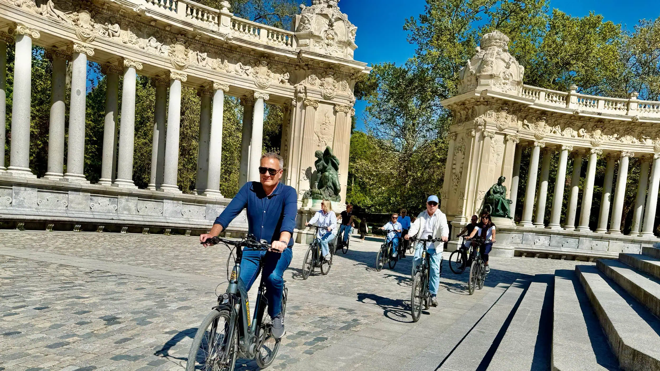 Kleine groep fietsers langs het monument van Alfonso XII in het Retiro Park, genietend van zonlicht, ruimte en elegantie tijdens een elektrische fietstour.